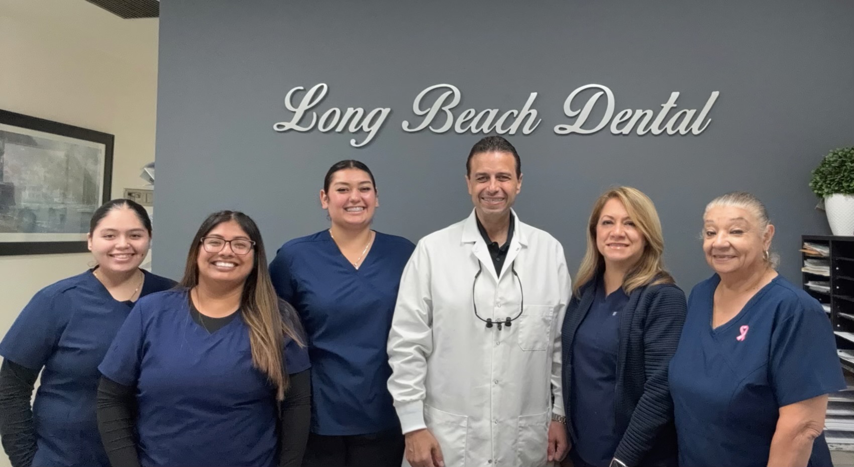 Long Beach Dental Practice team with Dr. Rezkalla and staff in front of office sign